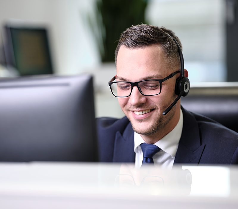 Mann mit Headset sitzt vor PC-Bildschirm und lächelt